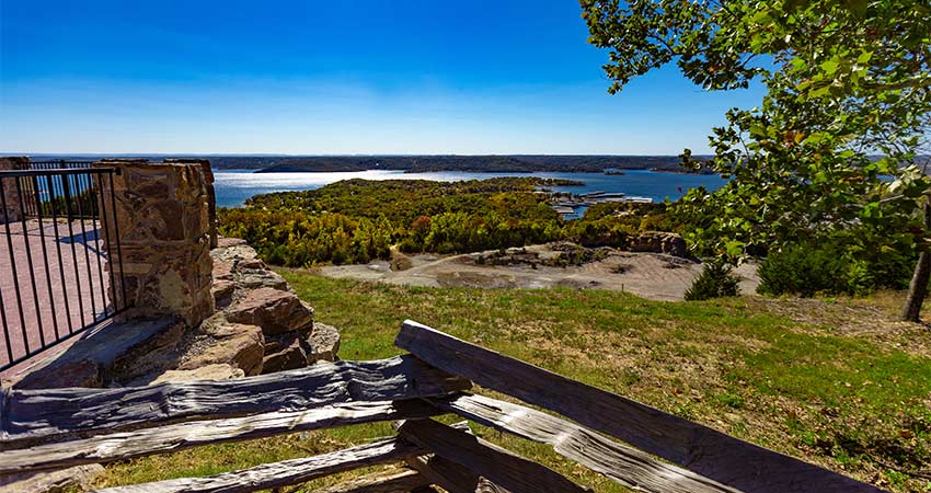 Blue sky view of Table Rock Lake from Baird Mountain framed by trees in foreground, Pink Jeep Tours Branson lookout point.