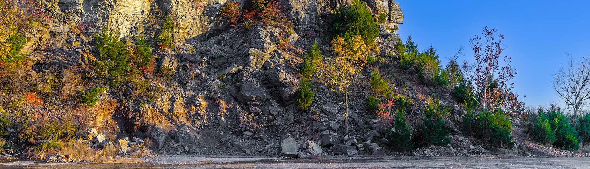 Autumn colored trees at the base of Baird Mountain’s cliffside against a deep blue sky, Baird Mountain Quarry, Branson.