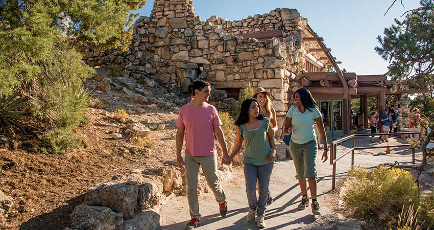 Four people walking along at path at Grand Canyon National Park with Hermits Rest in the background.