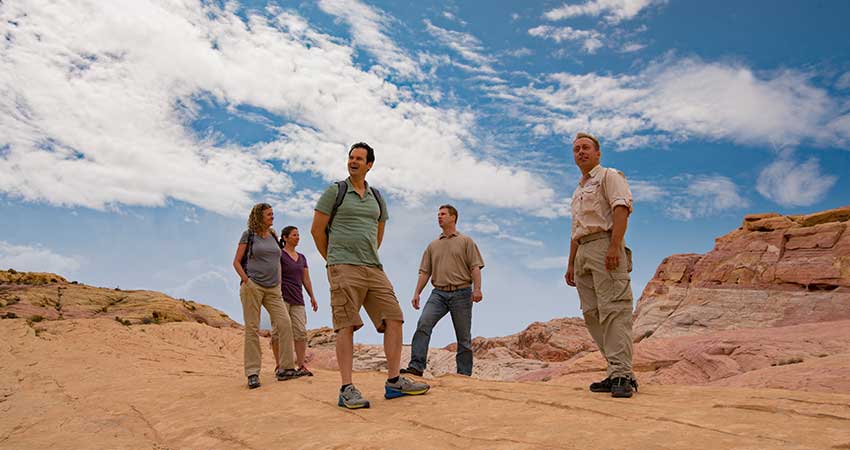 Pink Jeep Las Vegas tour guide and four guests standing on flat rock trail at Valley of Fire State Park in Nevada.