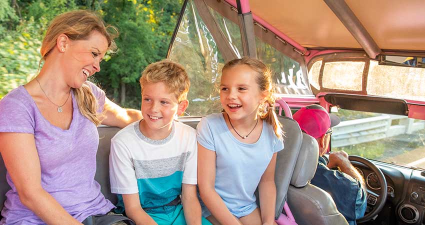 Mom and two kids smiling in back of a Pink Jeep, driven by Smoky Mountains adventure guide, Foothills Parkway tour.