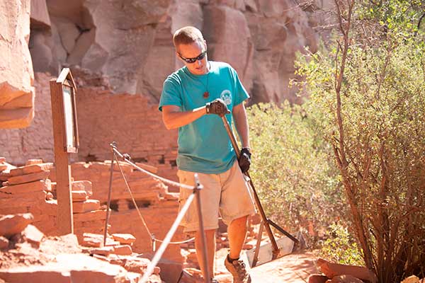 Pink Jeep Tours guide walking up rock steps and doing trail work at Honanki Heritage Site, Sedona, AZ.