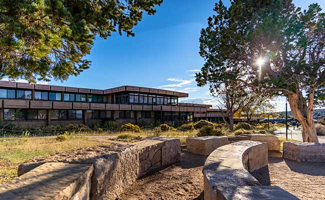 Sunbeam streams through trees in front of Thunderbird Lodge with pathway in foreground, Grand Canyon National Park, USA.