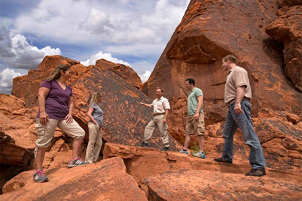 Pink Jeep tour guide explaining ancient petroglyphs to visitors at Valley of Fire State Park, NV.